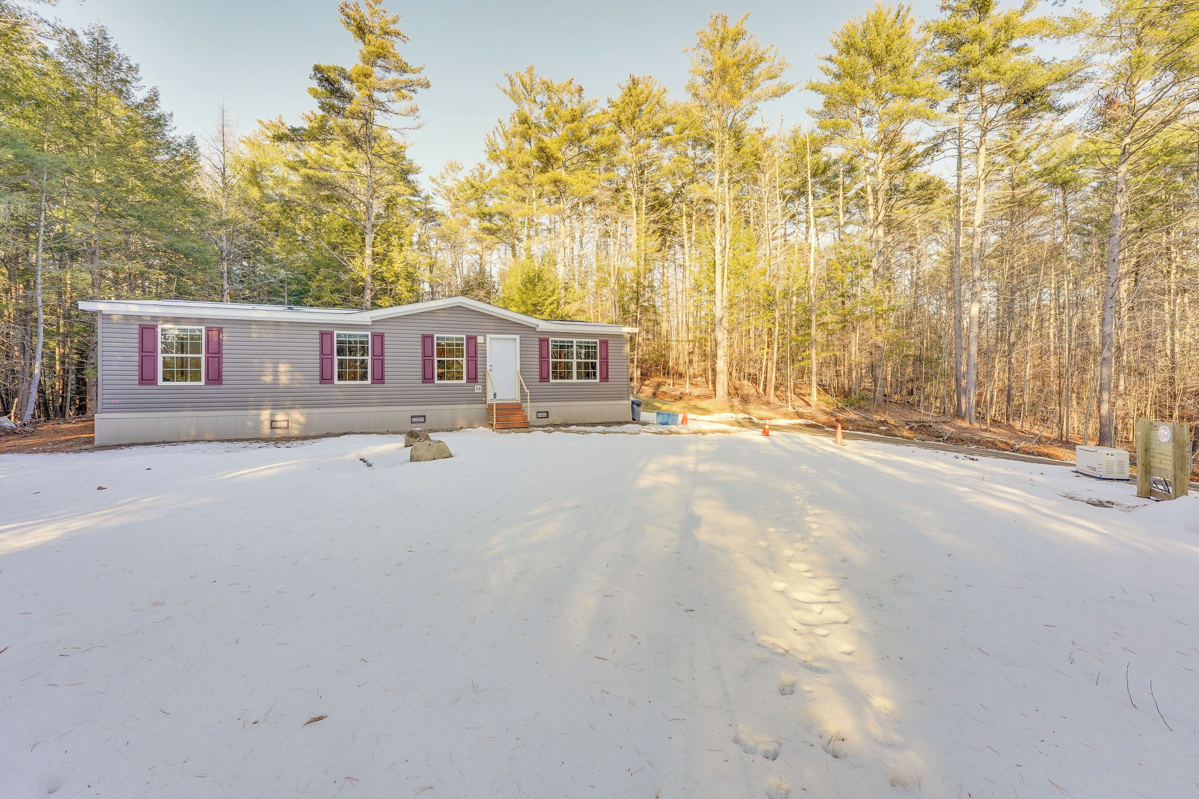 A single-story cabin with a covered porch, surrounded by a snowy landscape and dense forest.