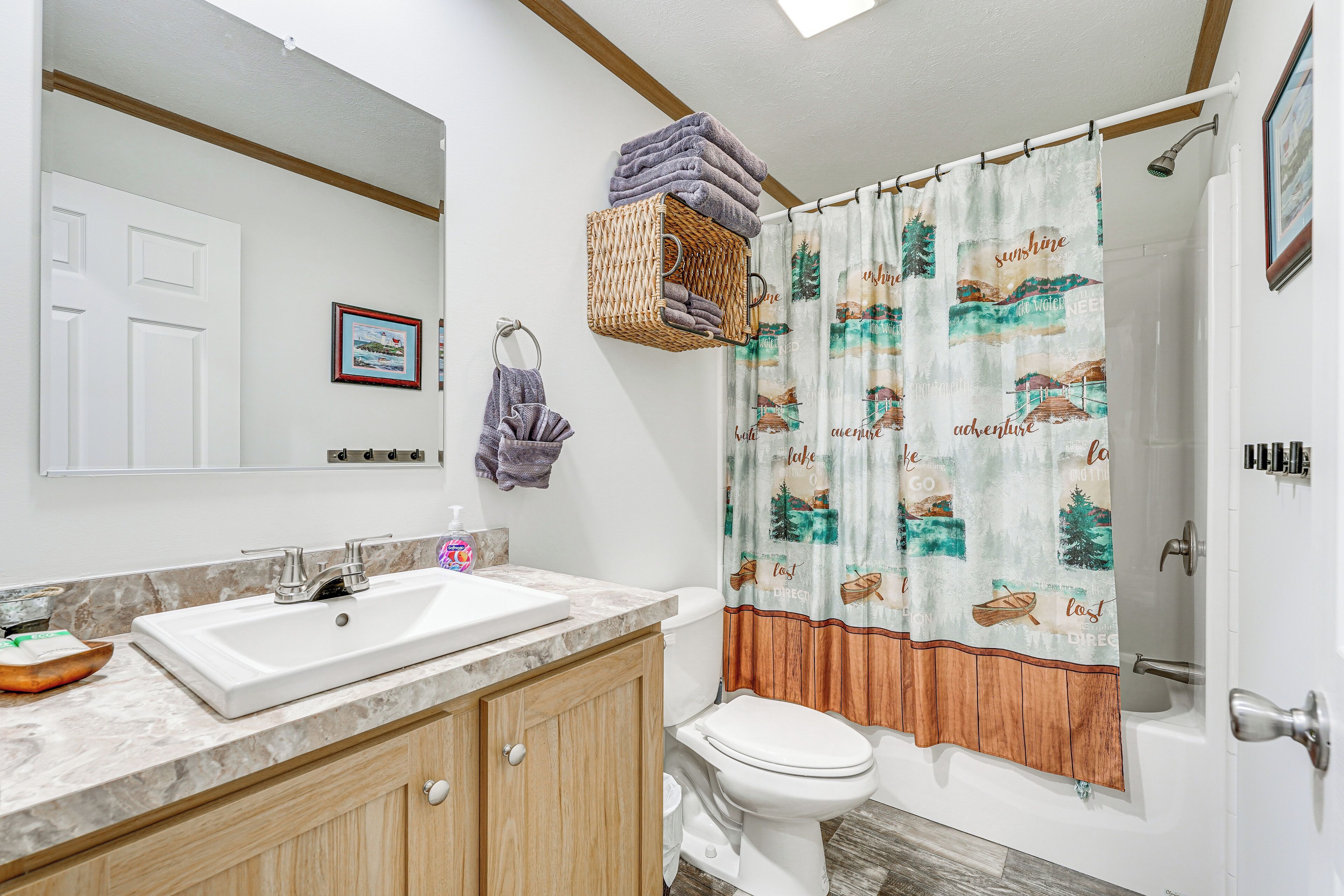 A bathroom with a white sink, wooden cabinets, a white toilet, and a shower curtain with a nature theme.