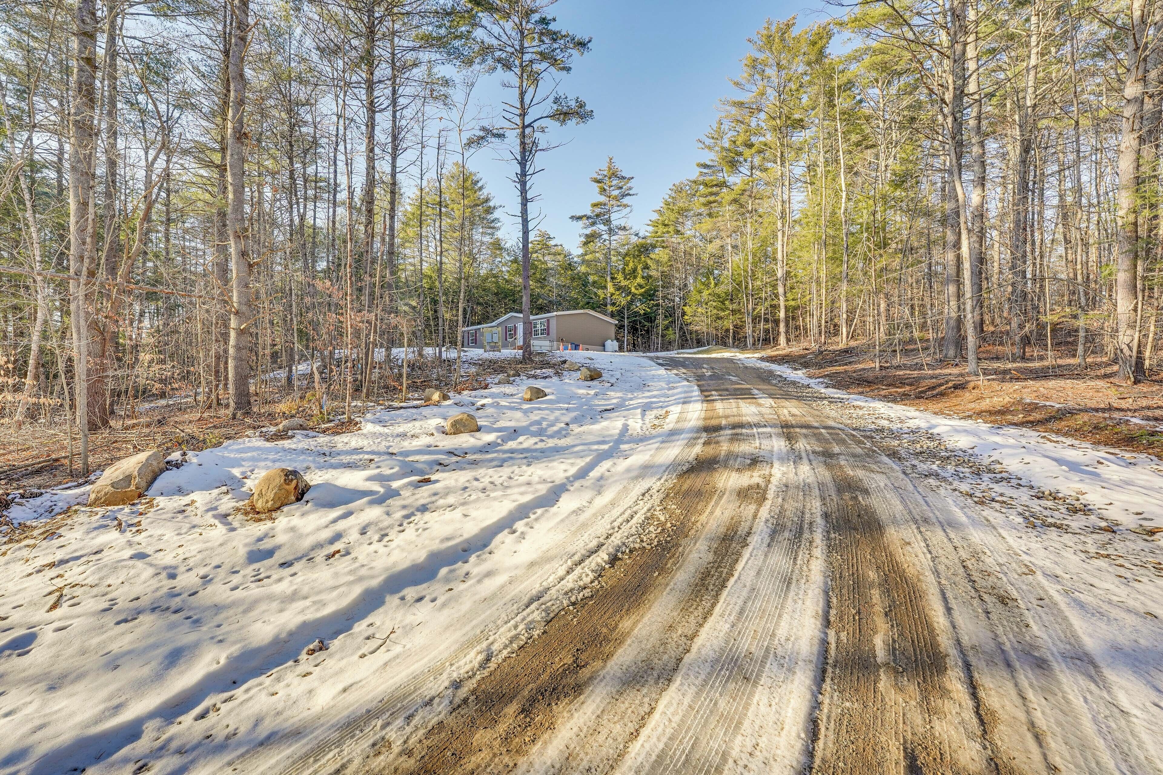 A snow-covered road leading to a cabin surrounded by trees.