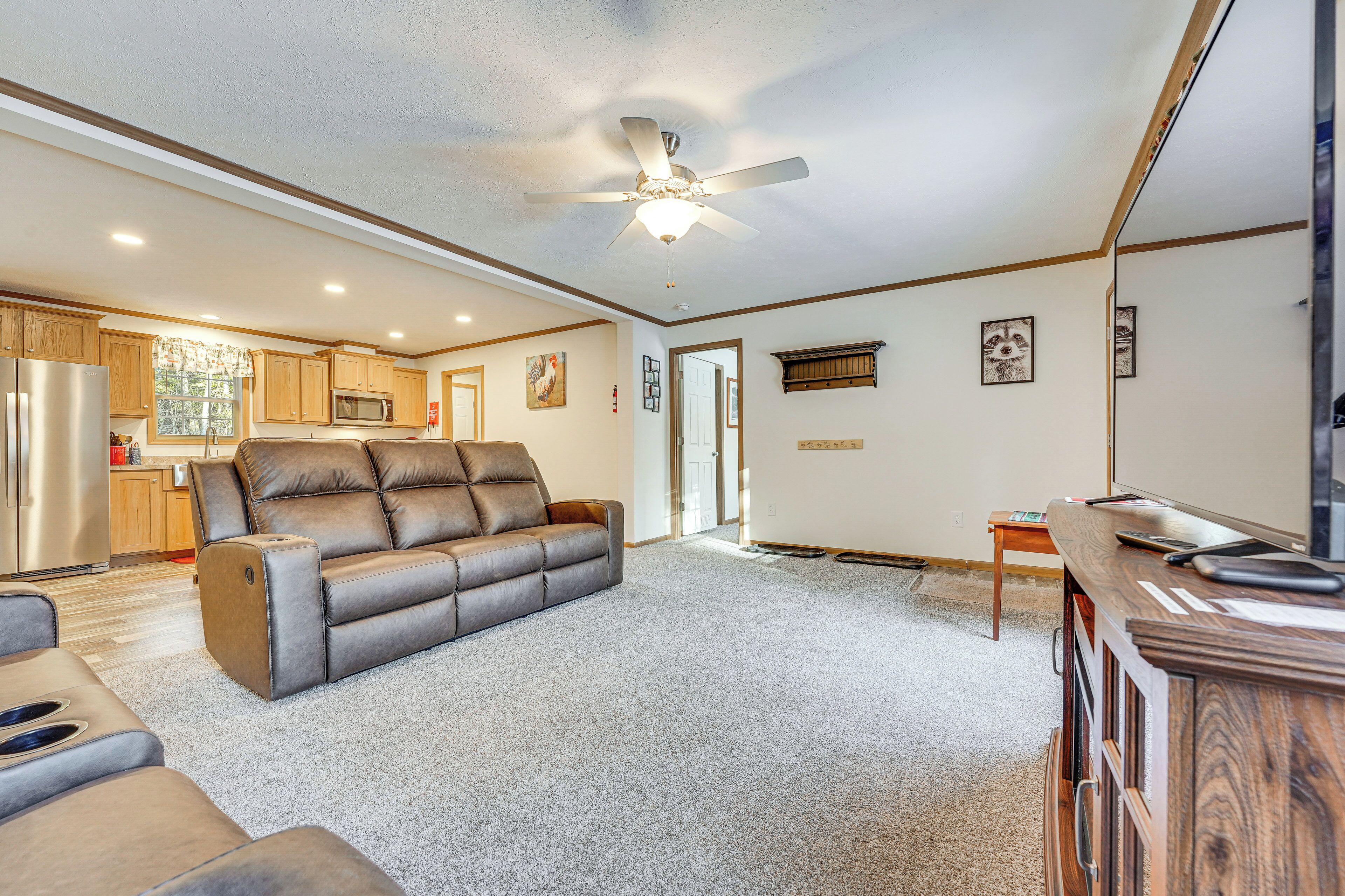 A spacious living area with a large leather sofa, a ceiling fan, and a kitchen in the background.