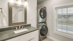 Un baño moderno con un espejo grande, un lavamanos y lavadoras apiladas.