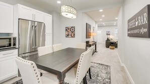 Una cocina moderna con gabinetes blancos, electrodomésticos de acero inoxidable y una zona de comedor con una mesa de madera oscura y sillas tapizadas.