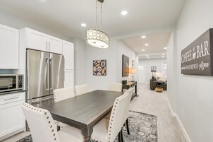 Una cocina moderna con gabinetes blancos, electrodomésticos de acero inoxidable y una zona de comedor con una mesa de madera oscura y sillas tapizadas.