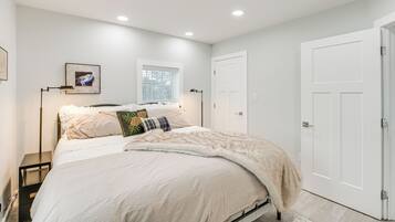 A bedroom with a bed, a nightstand, a framed picture on the wall, and a window with blinds.