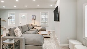 Una sala moderna con un sofá modular, una mesa de centro redonda y un televisor de pantalla plana montado en la pared.
