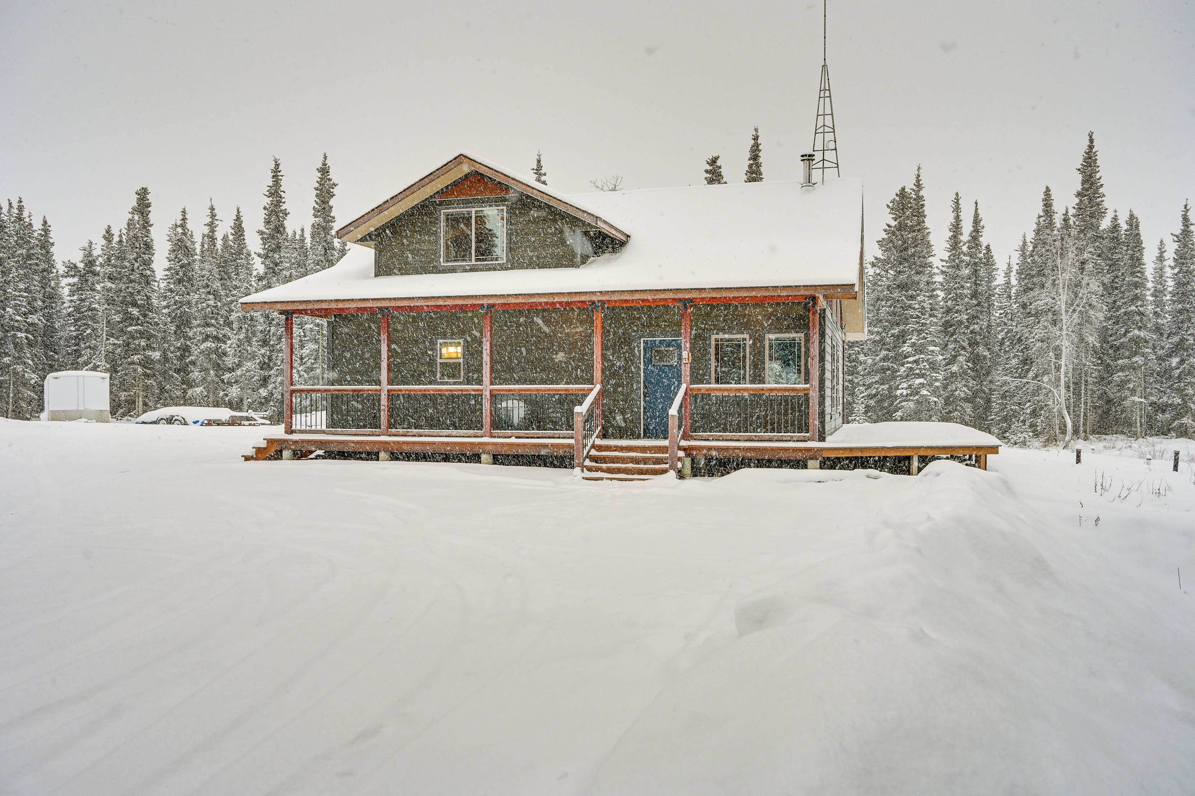 Un chalet enneigé, avec une façade en bois, de grandes fenêtres et un porche à l’avant.