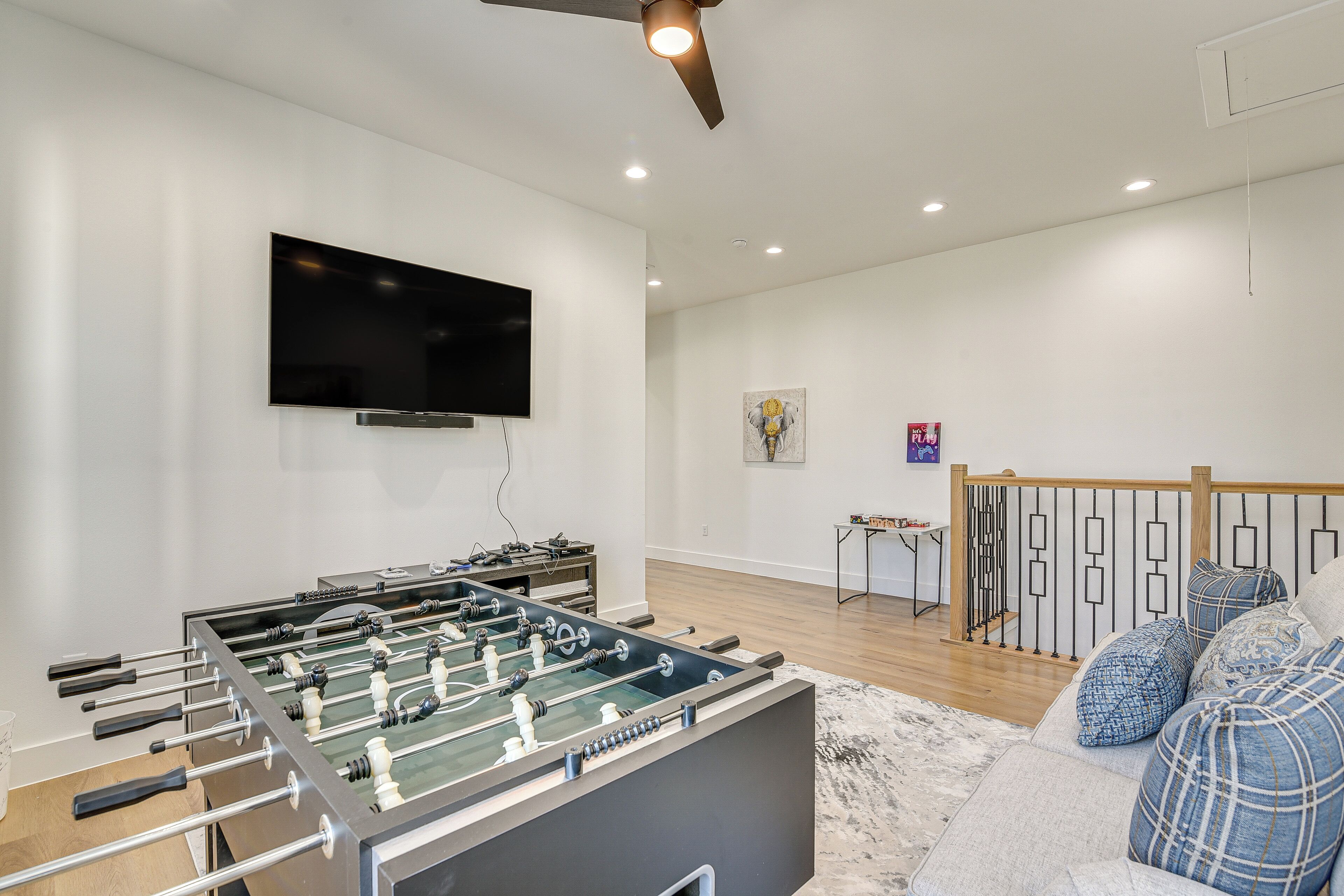 A modern living room with a foosball table, a flat-screen TV, and a staircase with a railing.