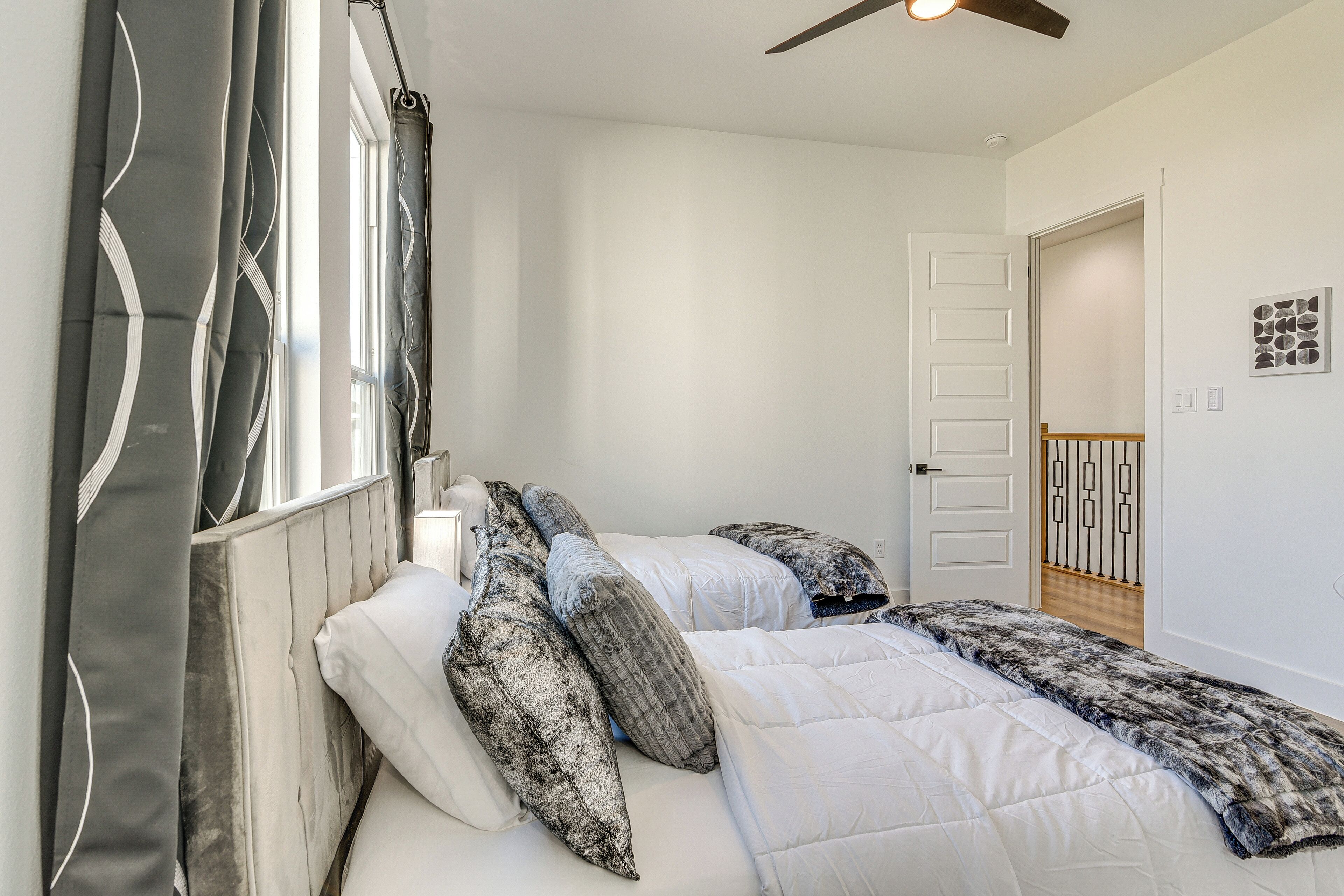 A bedroom with a bed, curtains, a ceiling fan, and a door leading to another room.