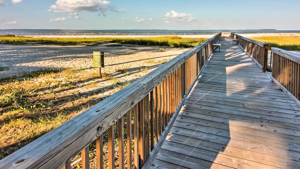 Une promenade en bois mène à une plage où un panneau indique les règles du parc.