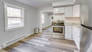 A modern kitchen with white cabinets, a stainless steel refrigerator, and a wood-patterned floor.