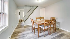 A dining area with a wooden table and chairs, a staircase, and a view of the outside.