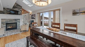 Un salon spacieux avec une cheminée, un coin repas avec une table en bois et une grande fenêtre donnant sur un lac.