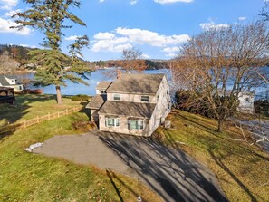 Ein zweistöckiges Haus mit Steinaußenwand, einer Auffahrt und Blick auf einen See.