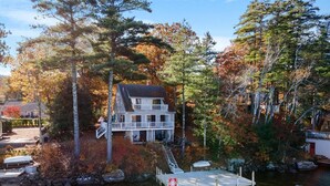 Ein zweistöckiges Haus mit einem Steg, der in einen See führt, umgeben von Bäumen in Herbstfarben.