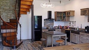 Uma cozinha moderna com escada de madeira, ilha central e parede decorativa em pedra.