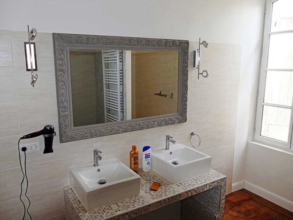 Un baño con dos lavamanos, un espejo grande y un secador de pelo en la pared.