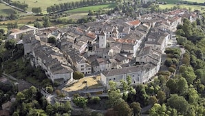 Vista aérea de uma cidade histórica com edifícios bem próximos, uma igreja imponente e campos verdes ao redor.