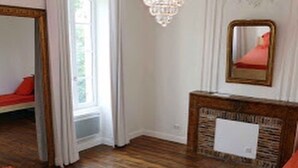 Quarto com piso de madeira, um espelho grande, um lustre e lareira com moldura de pedra.
