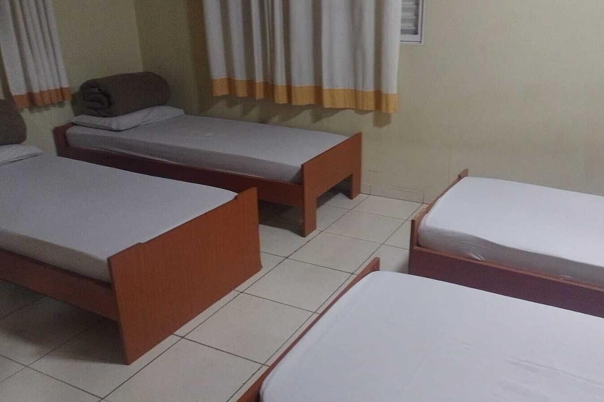 A room with three single beds, a small table, and a window with curtains.