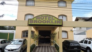 Entrada de un hotel con un letrero que dice "HOTEL BROOKLIN", destacando una fachada simétrica con ventanas arqueadas y una entrada central.