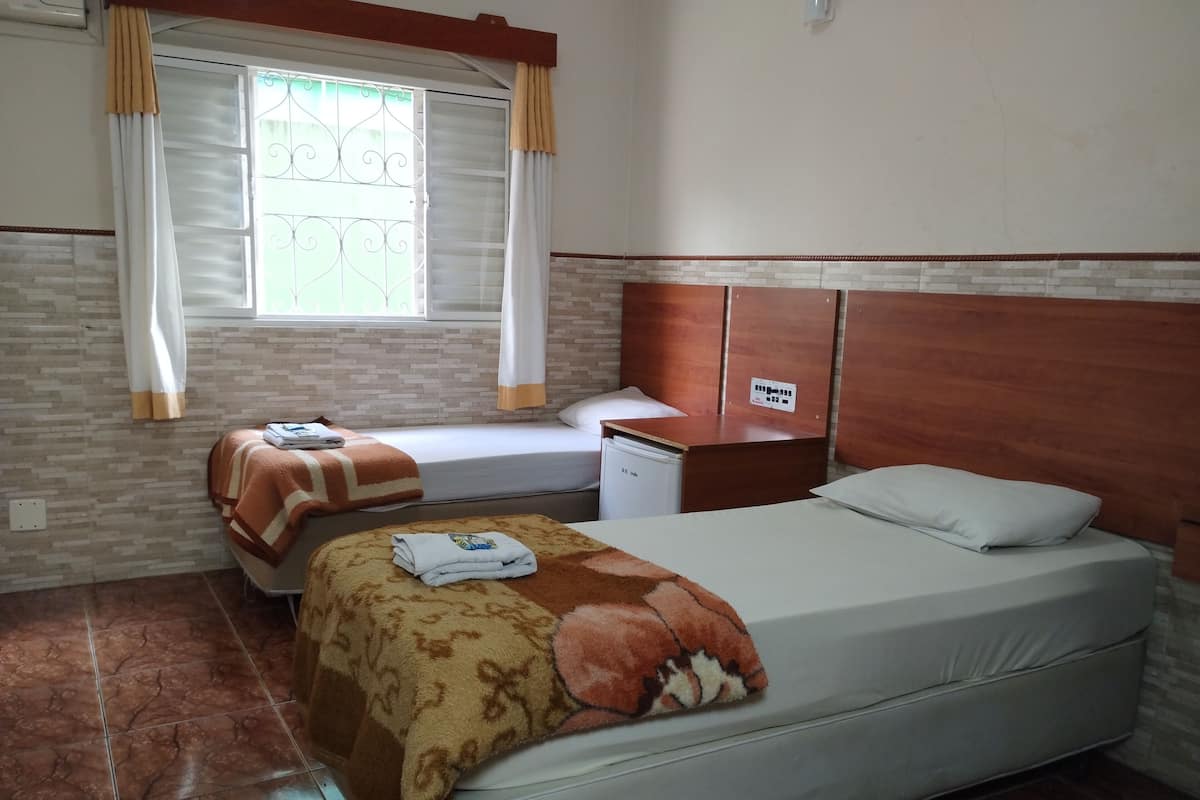 A hotel room with a bed, a small desk, a window with curtains, and a tiled floor.