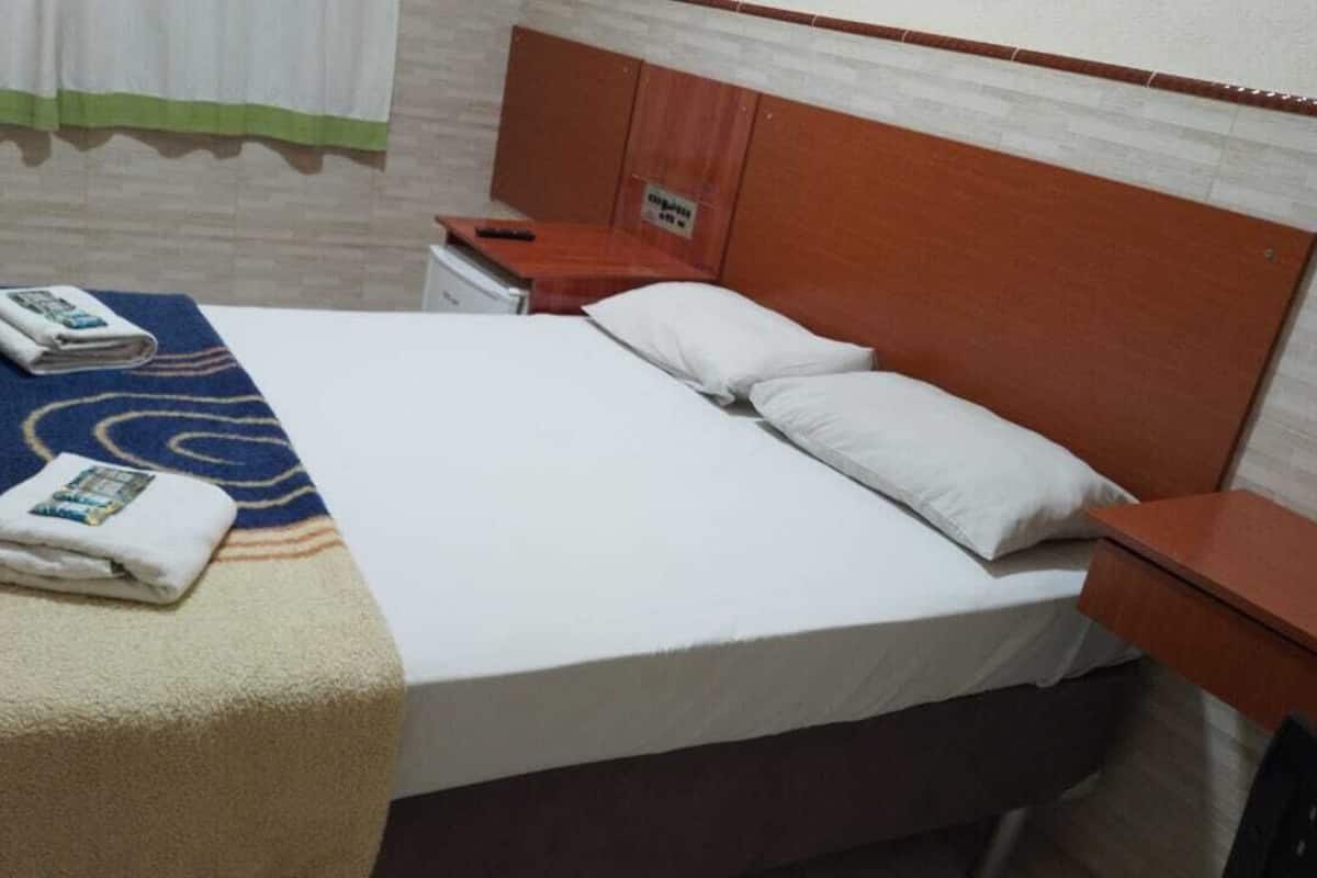 A hotel room with a bed, a nightstand, a wooden headboard, and a towel on the bed.
