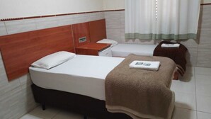 Habitación de hotel con cama, mesita de noche, una pequeña mesa, una silla y una ventana con cortinas.