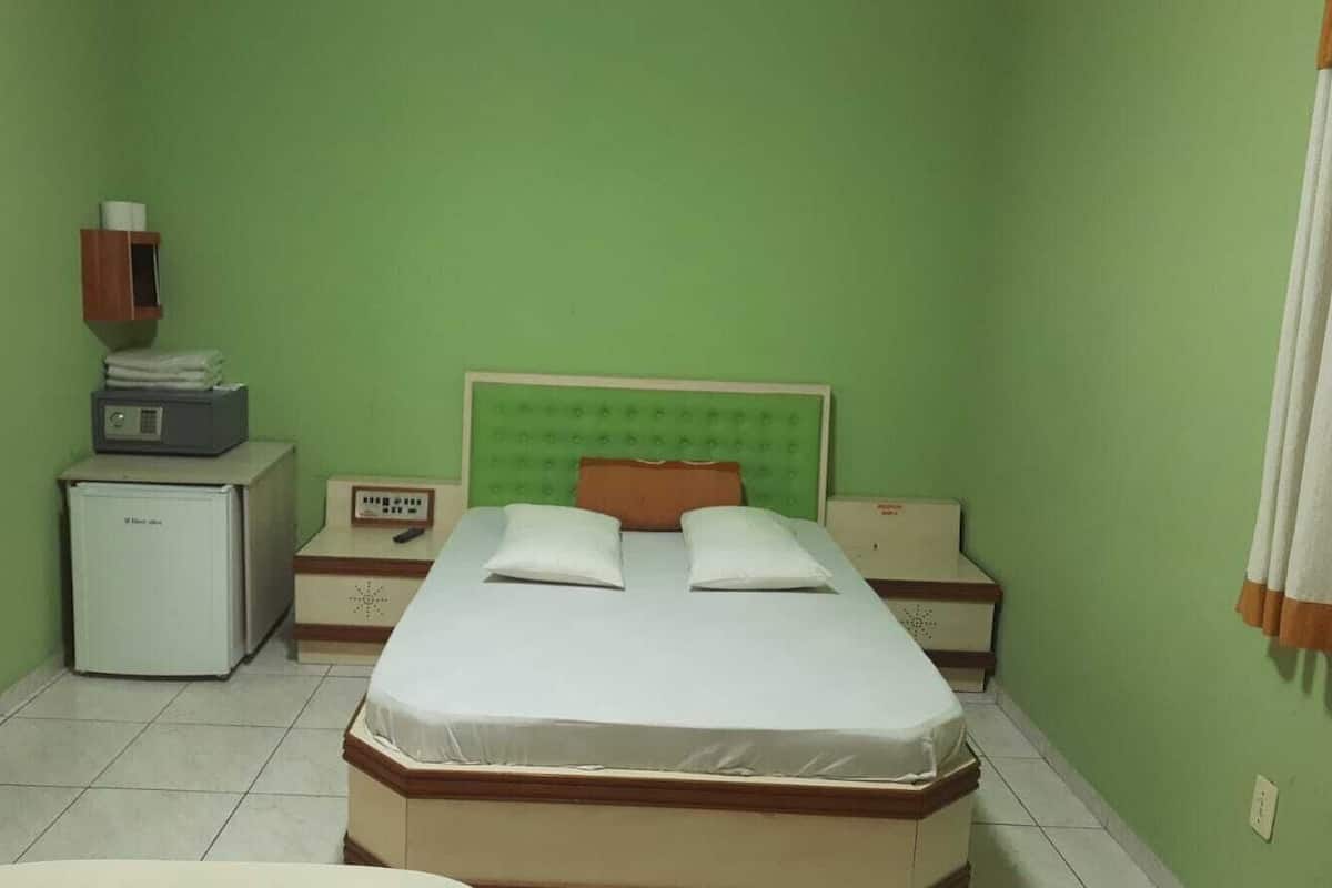 A small, clean room with a single bed, a nightstand, a small desk, and a refrigerator.