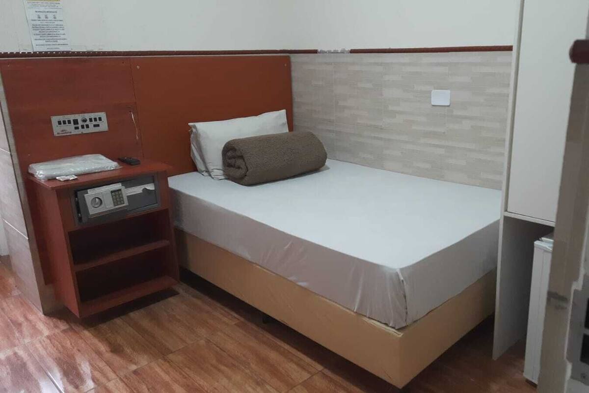A small, single-bed room with a wooden headboard, a bedside table with a radio, and a small cabinet.