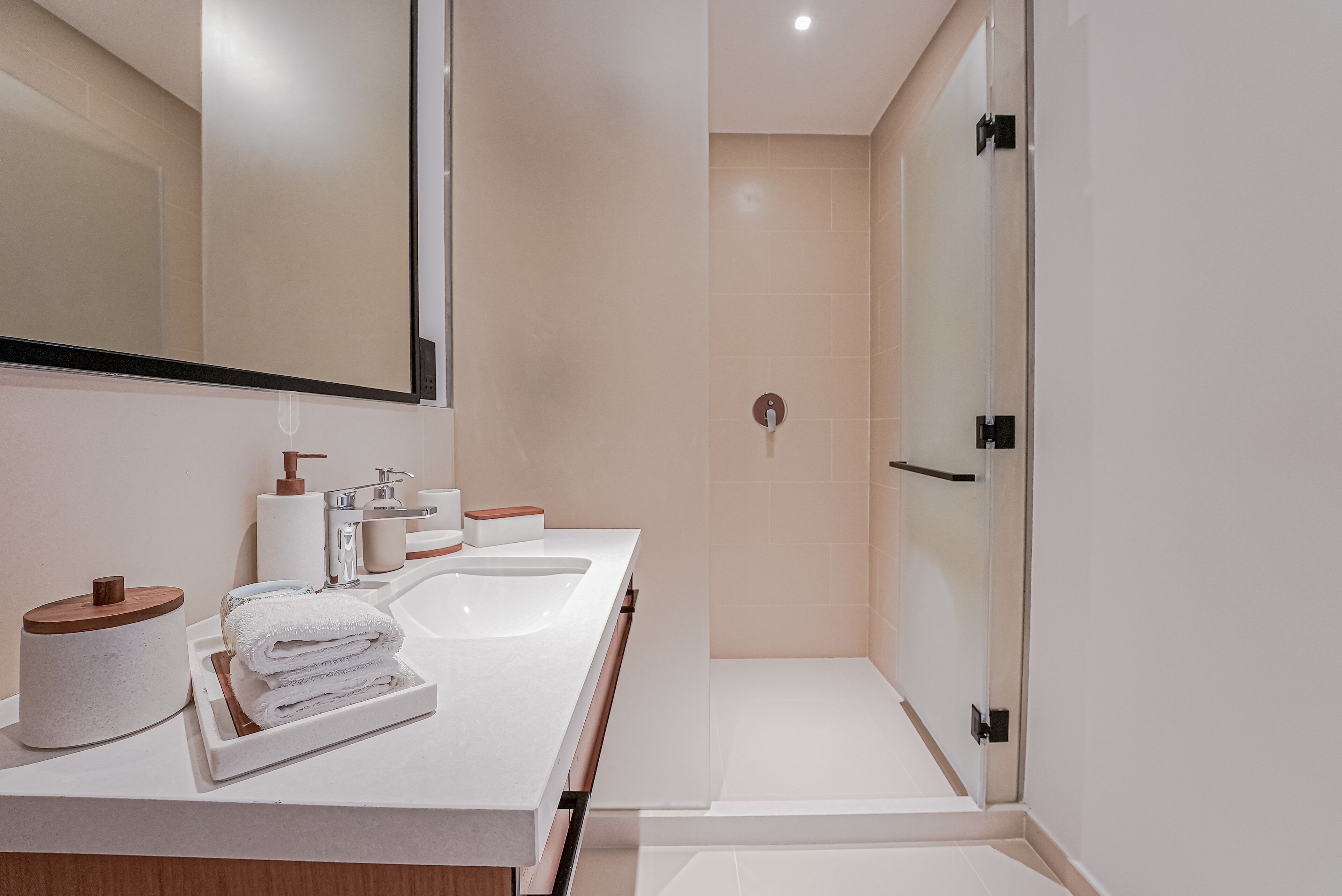 Une salle de bain moderne dotée d’un grand miroir, de deux lavabos, d’une douche et d’un meuble-lavabo avec des articles de toilette.