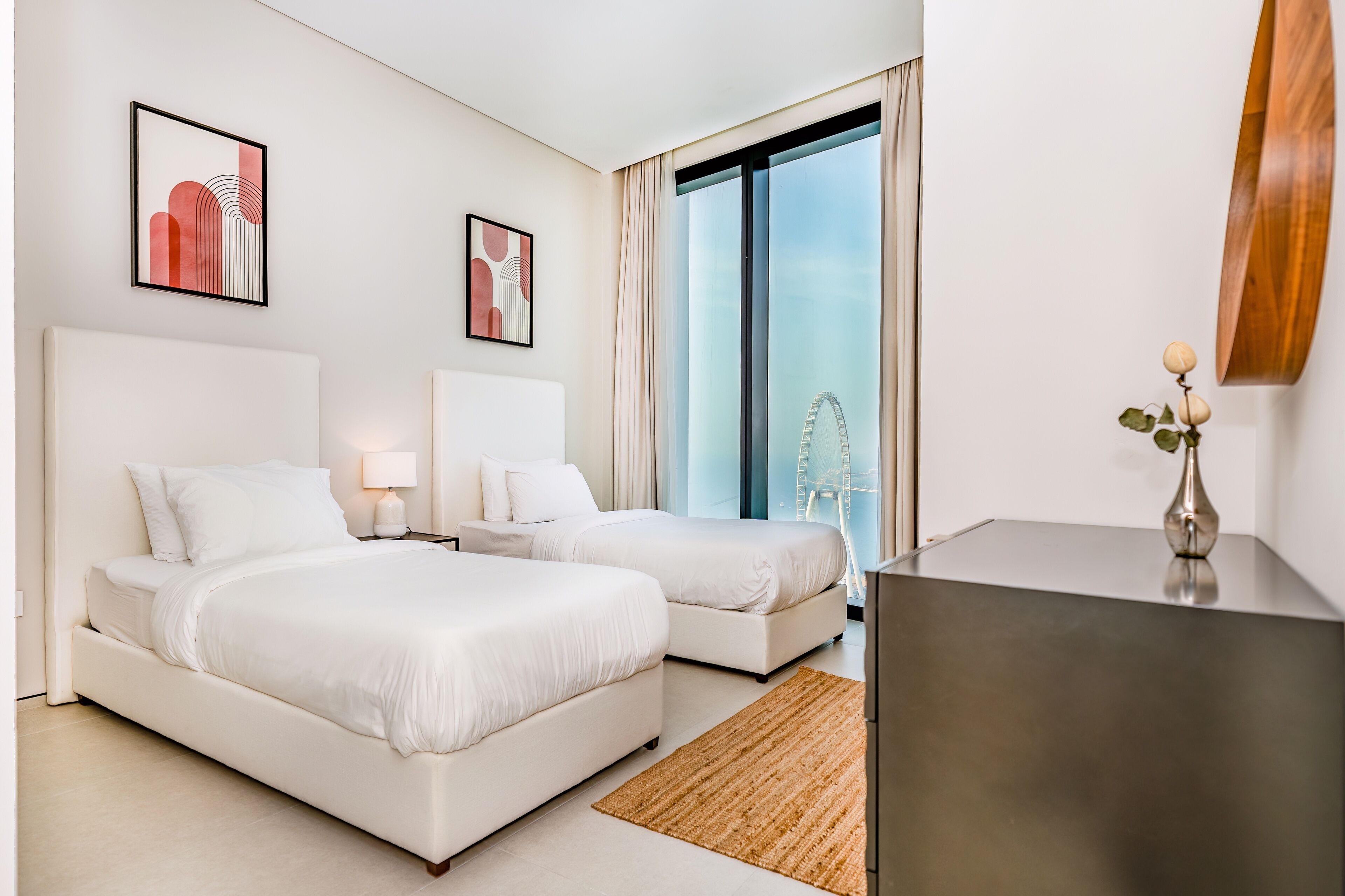 A modern hotel room with two beds, a desk, and a large window with a view of a Ferris wheel.