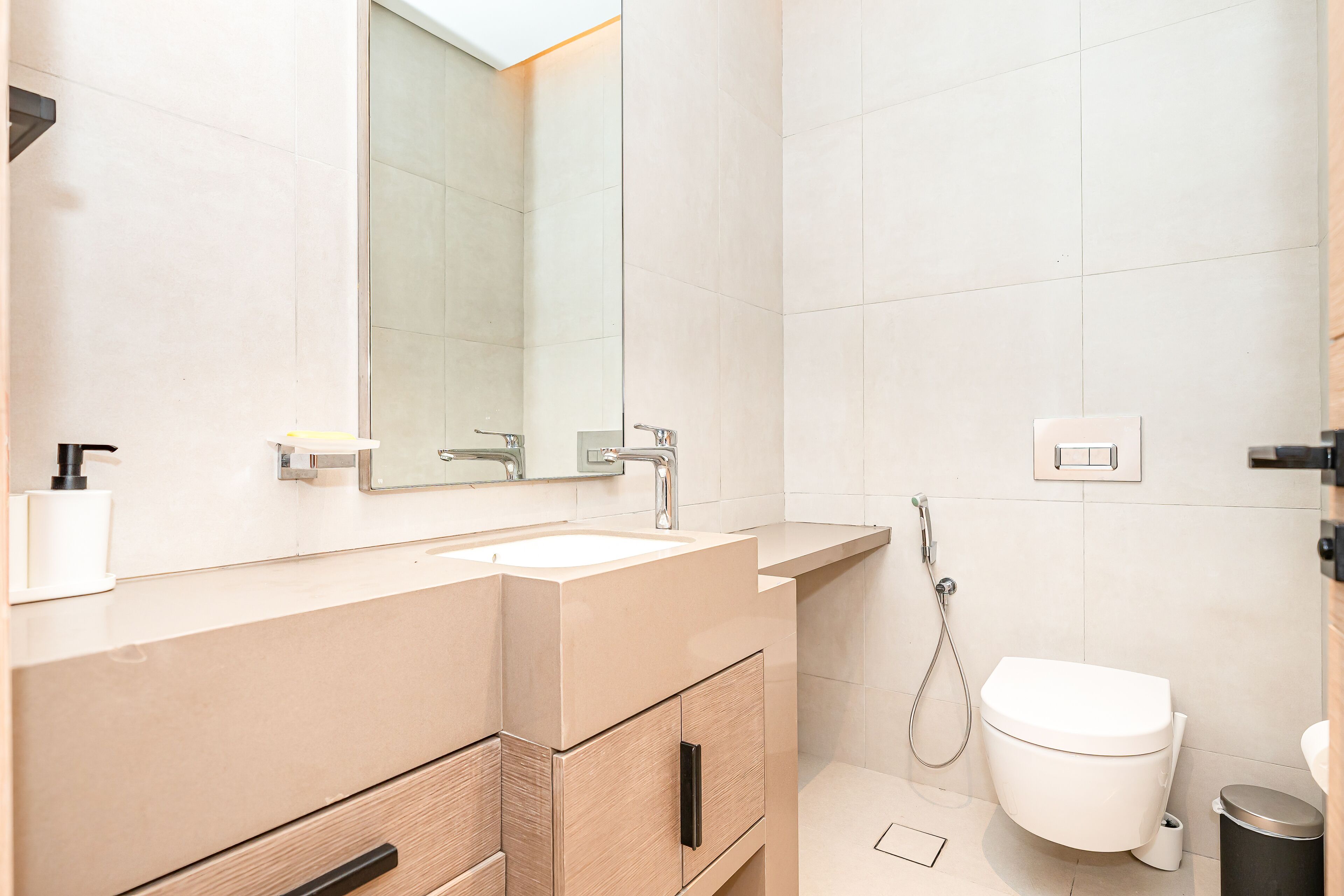 Ein modernes Badezimmer mit einem beigefarbenen Waschtisch, einem großen Spiegel, einem weißen Waschbecken, einer Toilette und einer Dusche.