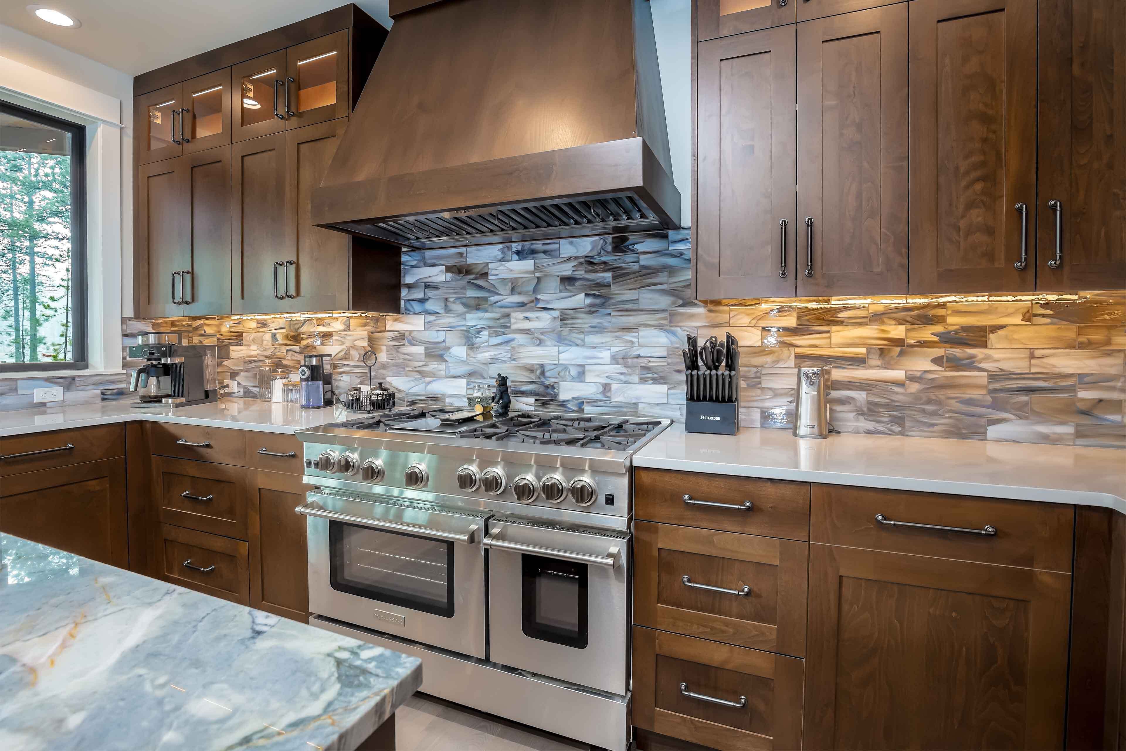 A modern kitchen with dark wood cabinets, a stone backsplash, and stainless steel appliances.