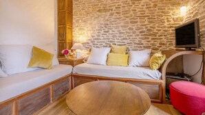 A cozy room with a stone wall, a wooden bench, a round table, and a television.