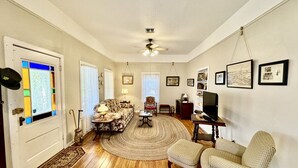 A spacious living room with hardwood floors, a large round rug, a sofa, a chair, a television, and framed pictures on the wall.