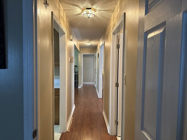 A hallway with wooden flooring, white walls, and doors on both sides.