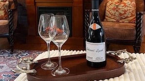 Un salon chaleureux avec une cheminée, un téléviseur fixé au-dessus et une bouteille de vin posée sur un plateau.