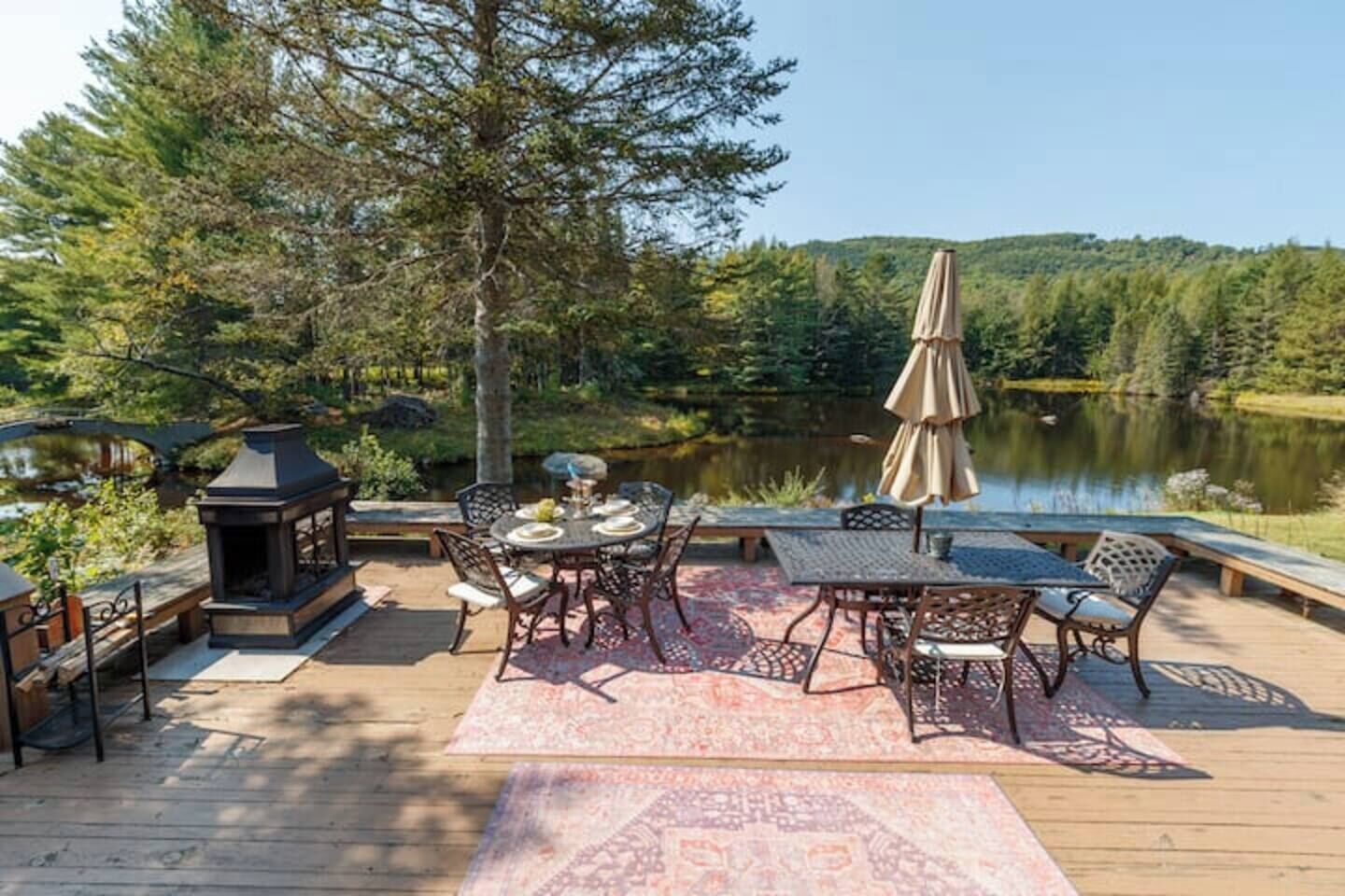 Une terrasse dotée de mobilier d’extérieur, d’un foyer et offrant une vue sur un lac entouré d’arbres.