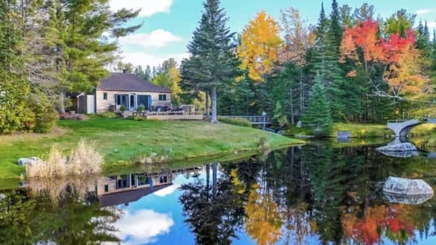 Une maison avec un étang devant, entourée d’arbres et sous un ciel dégagé.