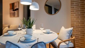 A dining area with a round table, white plates, bowls, wine glasses, and a potted plant. There is a round mirror on the wall and a brick wall to the right. - Longbeach Smart Muchavista (El Campello)