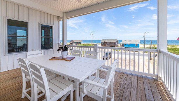 A covered outdoor area with a white table and chairs, a ceiling fan, and a view of the beach and ocean. - The Sandbar - Kitty Hawk MP 2.5, Semi Oceanfront, Ocean View, Elevator, Pool, Hot Tub (Kitty Hawk)