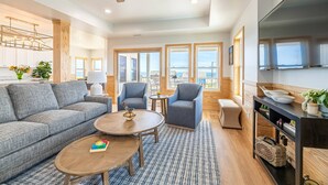 A spacious living room with a grey sofa, two armchairs, a coffee table, and a TV stand. - The Sandbar - Kitty Hawk MP 2.5, Semi Oceanfront, Ocean View, Elevator, Pool, Hot Tub (Kitty Hawk)