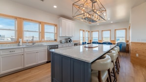 A modern kitchen with a large island, white cabinets, and a unique geometric chandelier. - The Sandbar - Kitty Hawk MP 2.5, Semi Oceanfront, Ocean View, Elevator, Pool, Hot Tub (Kitty Hawk)