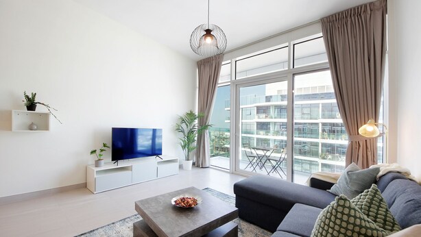 Una sala moderna con un televisor de pantalla plana, una mesa de centro con un cuenco, un sofá con cojines estampados y un ventanal con cortinas.
