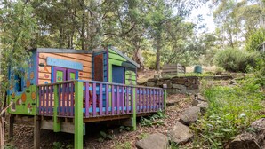 A colorful wooden playhouse with a purple and green fence, surrounded by trees and rocks. - Christensen - Pet Friendly home at the base of Mt Buller (Sawmill Settlement)