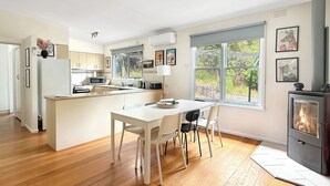A modern kitchen with a central island, a dining area with chairs, and a wood-burning stove. - Christensen - Pet Friendly home at the base of Mt Buller (Sawmill Settlement)