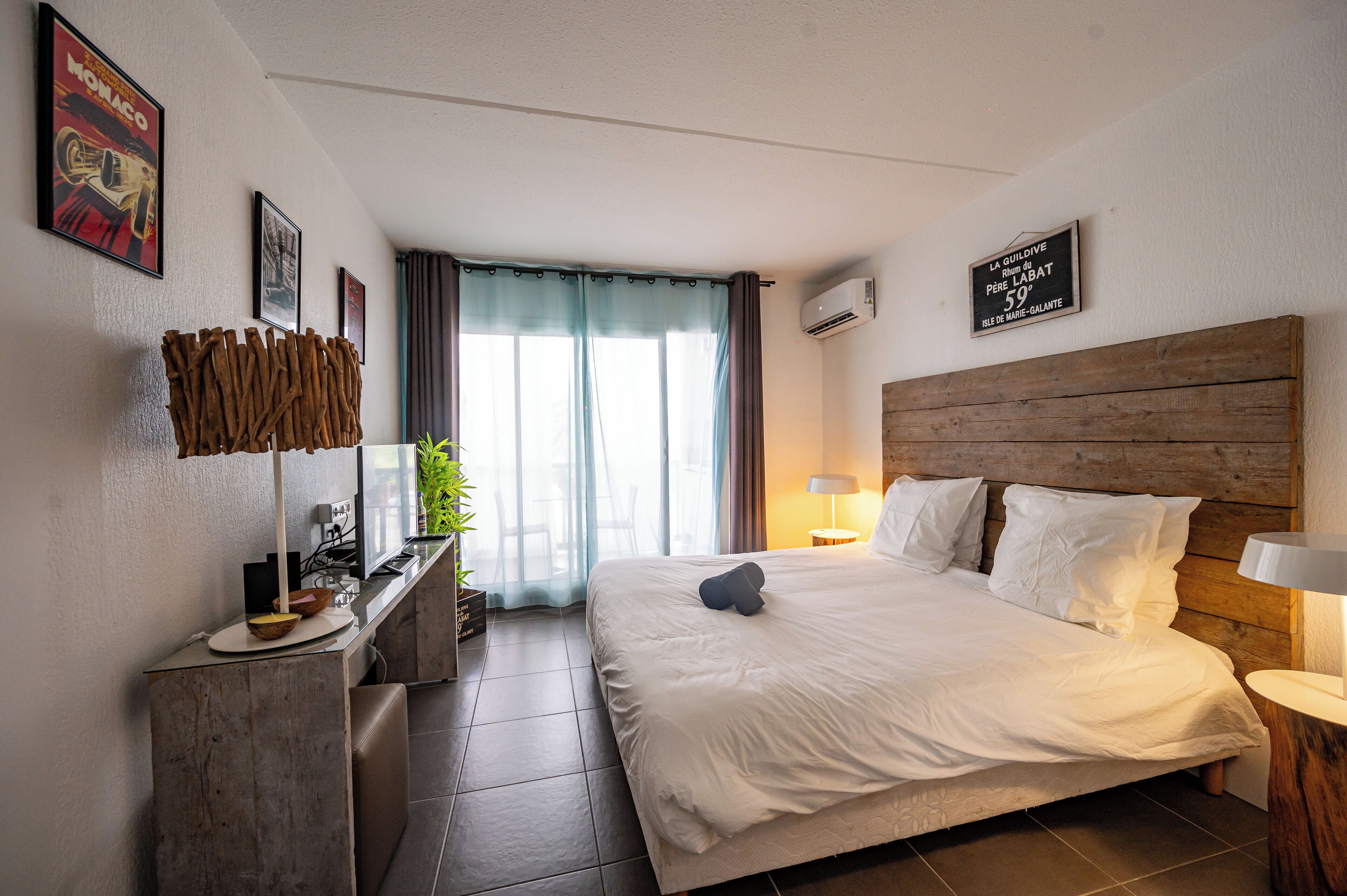 Hotellihuone, jossa on suuri sänky, työpöytä lampun kanssa, ikkuna verhoilla ja seinällä kyltti.