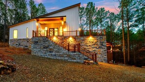 A modern house with a stone staircase leading to a wooden deck, surrounded by trees.