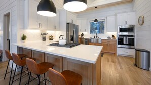 A modern kitchen with white cabinetry, a central island with bar stools, stainless steel appliances, and pendant lighting.