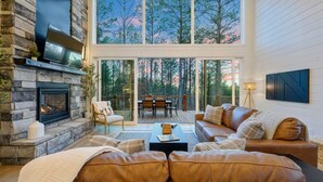 A spacious living room with a stone fireplace, leather sofas, and a large glass door leading to an outdoor deck.